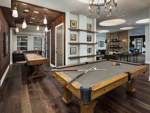 A pool table in a room with a wooden floor and a brick wall.