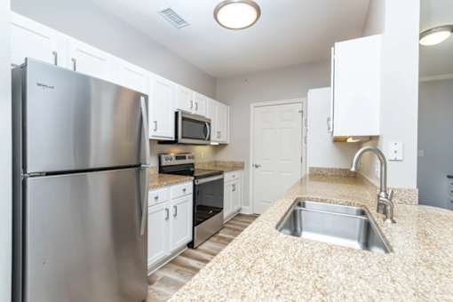 A kitchen with a stainless steel refrigerator and a sink with granite countertops.