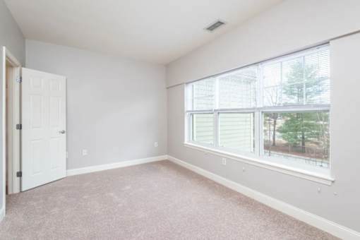 A room with a carpeted floor and a large window with blinds.