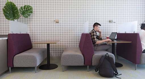 A man is sitting at a table with a laptop in a room with purple chairs.