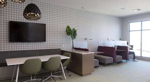A modern office space with a white table, grey chairs, and a television mounted on the wall.