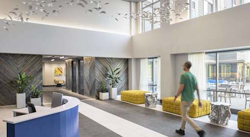 A man in a green shirt walks through a brightly lit office lobby.