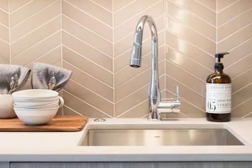 A kitchen sink with a faucet and a bottle of Cabot Hill Estate Dish Soap.
