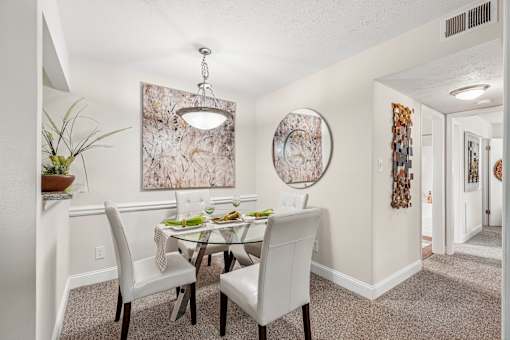 A dining room with a table set for two and a large abstract painting on the wall.