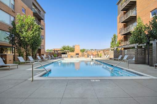 A swimming pool surrounded by lounge chairs and apartment buildings.