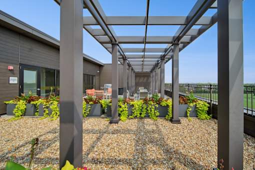 A building with a grey roof and a metal pergola over a gravel area with plants.