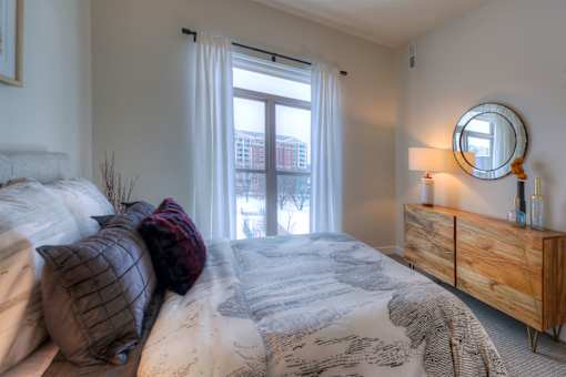 A bedroom with a bed, pillows, a nightstand, and a window.