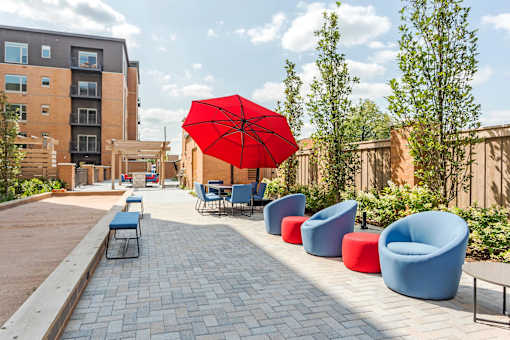 A red umbrella is in the middle of a row of blue and red chairs.
