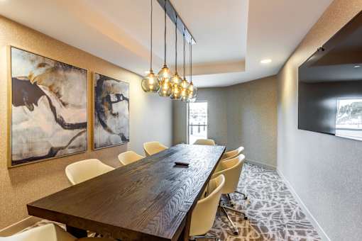 A long wooden table is surrounded by chairs in a room with a painting on the wall.