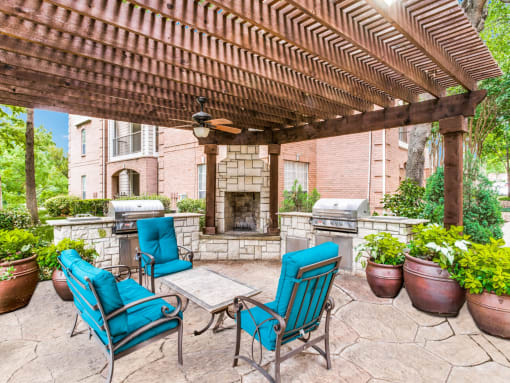 Luxury Apartments in North Dallas TX- Outdoor Patio With Fireplace, Two Grills, and Comfortable Blue Outdoor Chairs