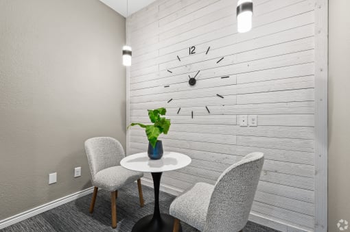a small table with two chairs in front of a wall with a clock on it