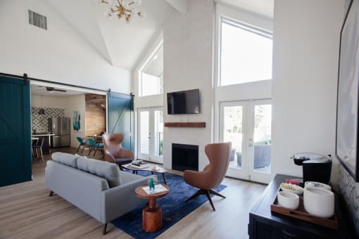 Mountain Park Apartments - MiLO at Mountain Park - Clubhouse with High Ceilings, Wood-Style Flooring, Area Rug, Couch, Armchairs, Coffee Station, and Fireplace