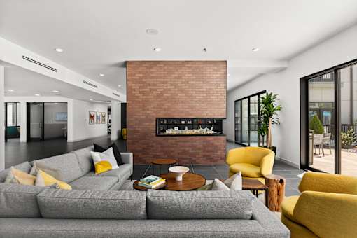 A grey couch with a yellow chair and a fireplace in the middle of the room.