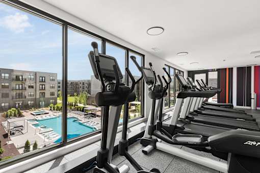 A gym with treadmills and a view of a pool and buildings outside.