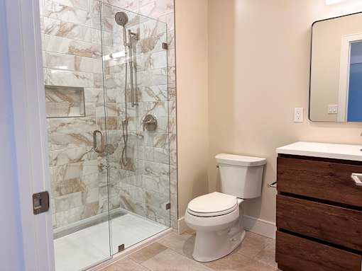 A white toilet sits next to a walk-in shower with a marble tile wall.