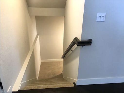 a stairway with a black railing and a white wall and stairs