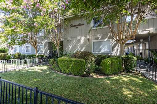 the exterior of an apartment building with a lawn and trees
