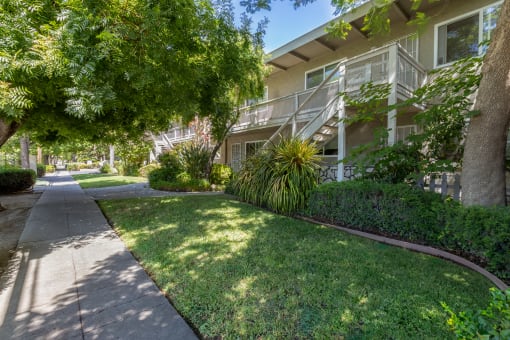 a sidewalk in front of an apartment building with grass and trees