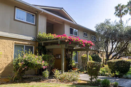 the front of a tan house with pink flowers on it