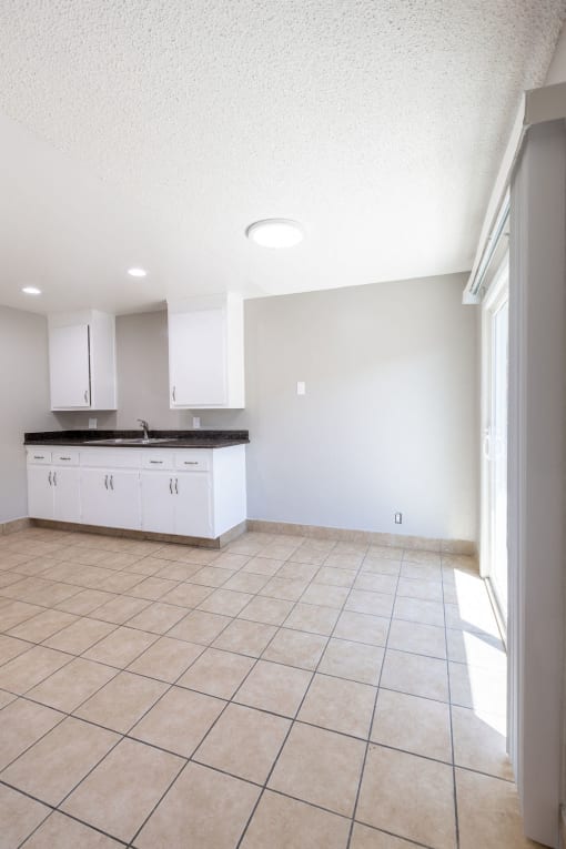 an empty kitchen with white cabinets and a tiled floor