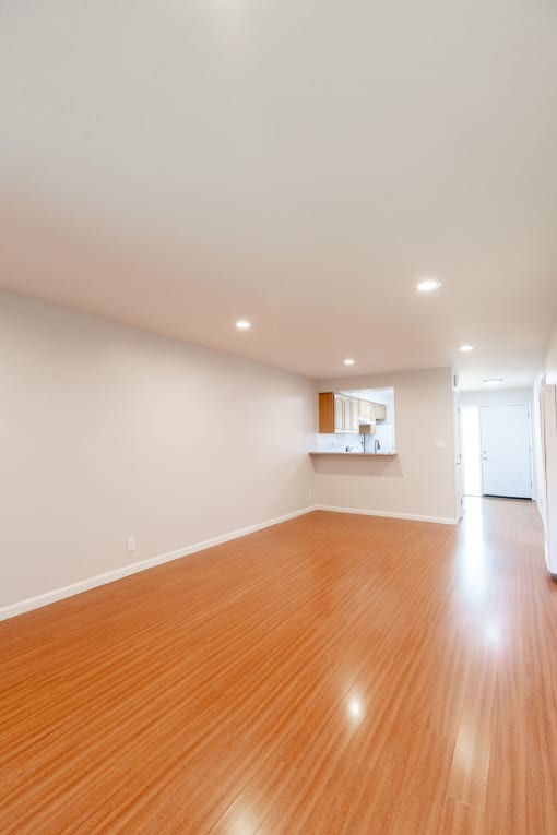 an empty living room with wood floors and a kitchen