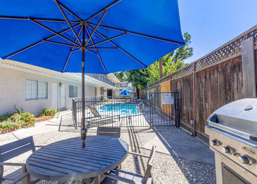 a patio with a blue umbrella and a swimming pool