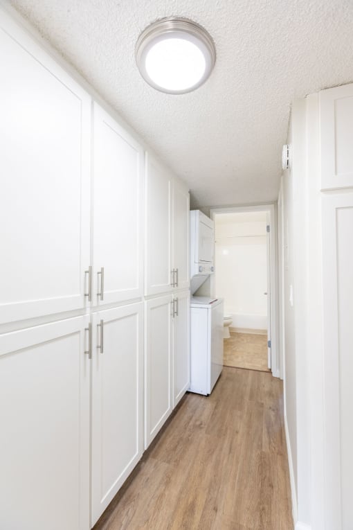 a long white kitchen with white cabinets and wood floors