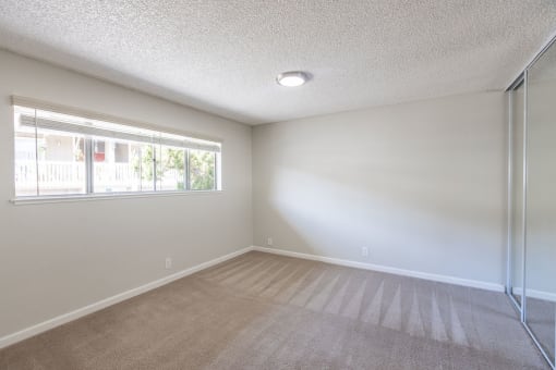 an empty living room with a large window and a mirrored closet
