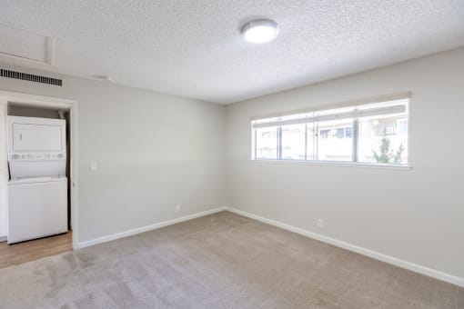 an empty living room with a window and a white kitchen