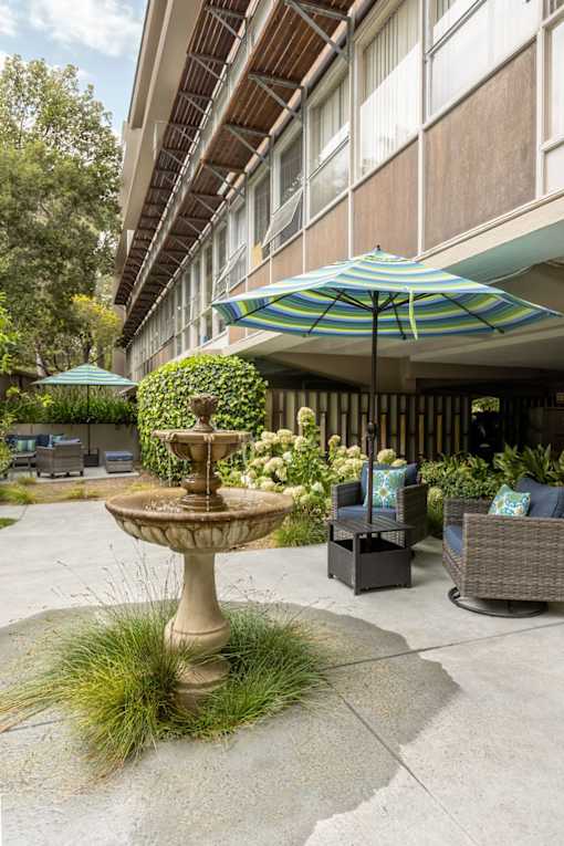 A patio with a fountain, chairs, and umbrellas.