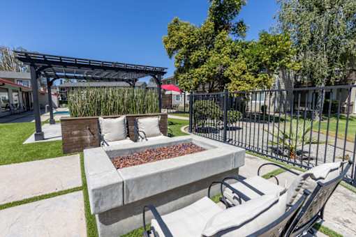 a patio with a fire pit and chairs in front of a fence
