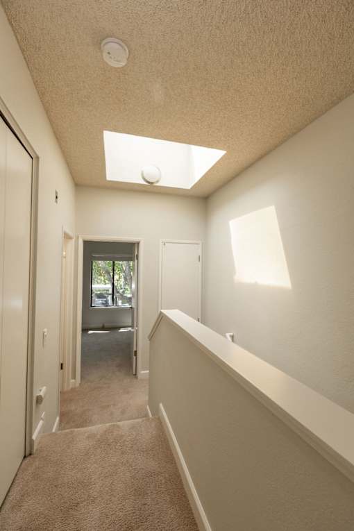 a hallway with a carpeted floor and a door to a room with a staircase