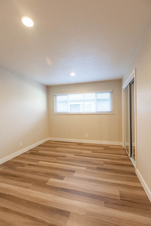 A room with wooden flooring and a window with blinds.