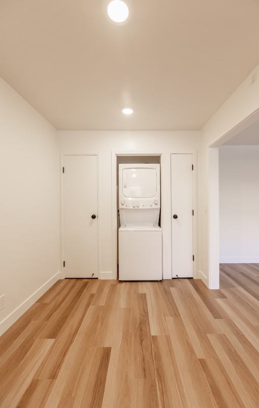 A white cabinet with a glass door is in the middle of a room with wooden floors.