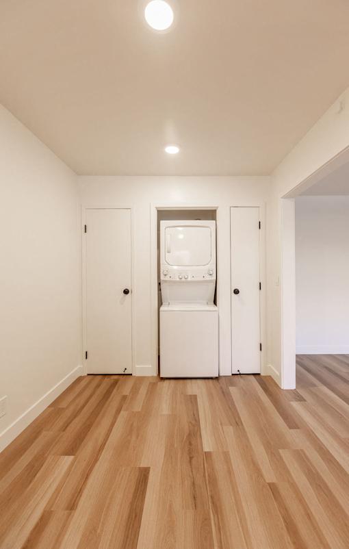 A white cabinet with a glass door is in the middle of a room with wooden floors.
