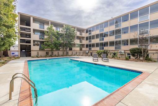 A swimming pool in front of a building with a sunny day.