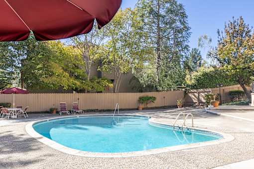 A red umbrella shades a swimming pool.