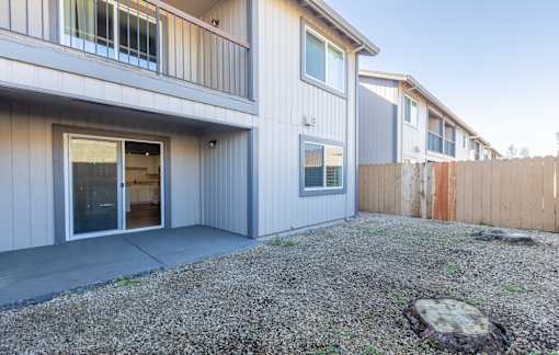 A grey house with a brown fence and a gravel driveway.