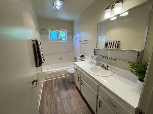 A bathroom with a toilet, sink, mirror, and a window.