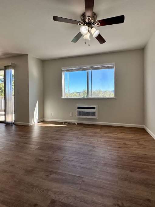 an empty living room with a ceiling fan and a window