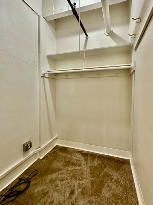 a walk in closet with white walls and a brown carpet