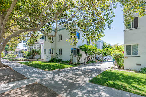 a white apartment building with trees and a sidewalk