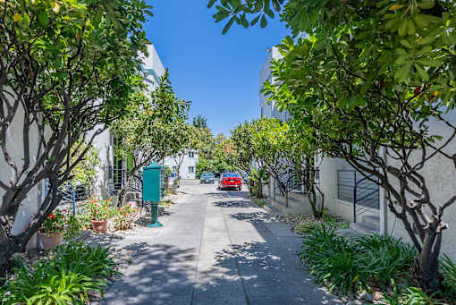 a red car is driving down a street between two white buildings