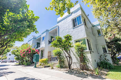 a white apartment building with trees and a sidewalk
