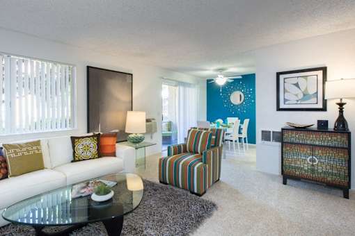 A living room with a white couch, a striped armchair, and a glass coffee table.