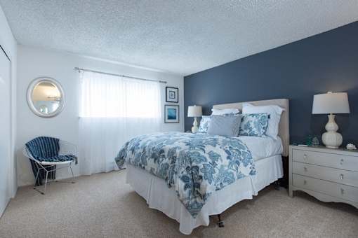A bedroom with a bed, chair, and lamp.