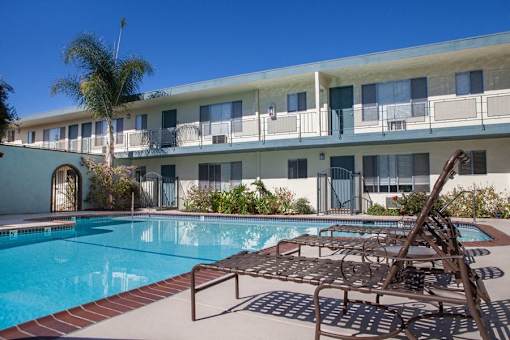 A pool area with sun loungers and a building in the background.
