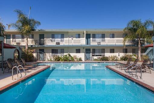 A swimming pool in front of a building with palm trees.