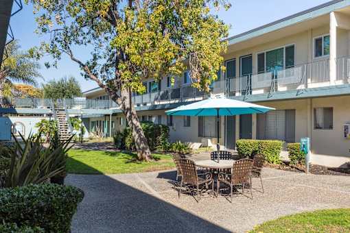 A patio with a table and chairs is surrounded by a building and trees.