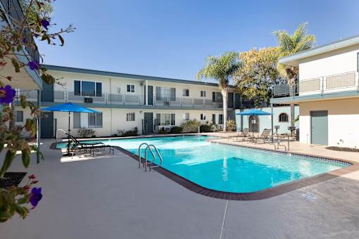A swimming pool in front of a building with a blue umbrella.